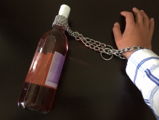 A close-up shot of a male's hand chained to a bottle of alcohol