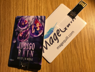 Two USB sticks of the e-book Indigo Rain on a table, the left one displaying the front with the cover and the right one with the official logo of MageQuill on the back, with the words 'magequill.com' written underneath