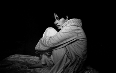 Black and white portrait of a male clutching his knees on the bed and staring at the camera after a nightmare