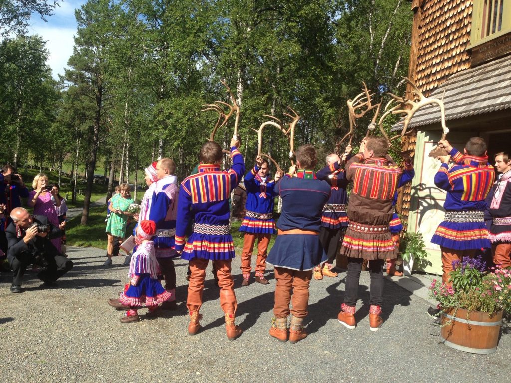A group men dressed in traditional blue-and-red Sami outfits dancing in a wedding in Swedish Lapland